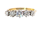 A five-stone diamond ring with a yellow gold band and silver-toned settings, featuring four round diamonds and a center oval diamond, shown on a plain white background.