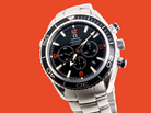 Omega x Swatch Chassis Automatic watch with a black dial, silver stainless steel case and bracelet, and orange accents, set against a solid orange background.