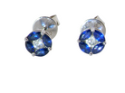 A pair of round stud earrings featuring deep blue gemstones in a four-petal arrangement with a clear center stone, set in silver-toned metal on a plain white background.