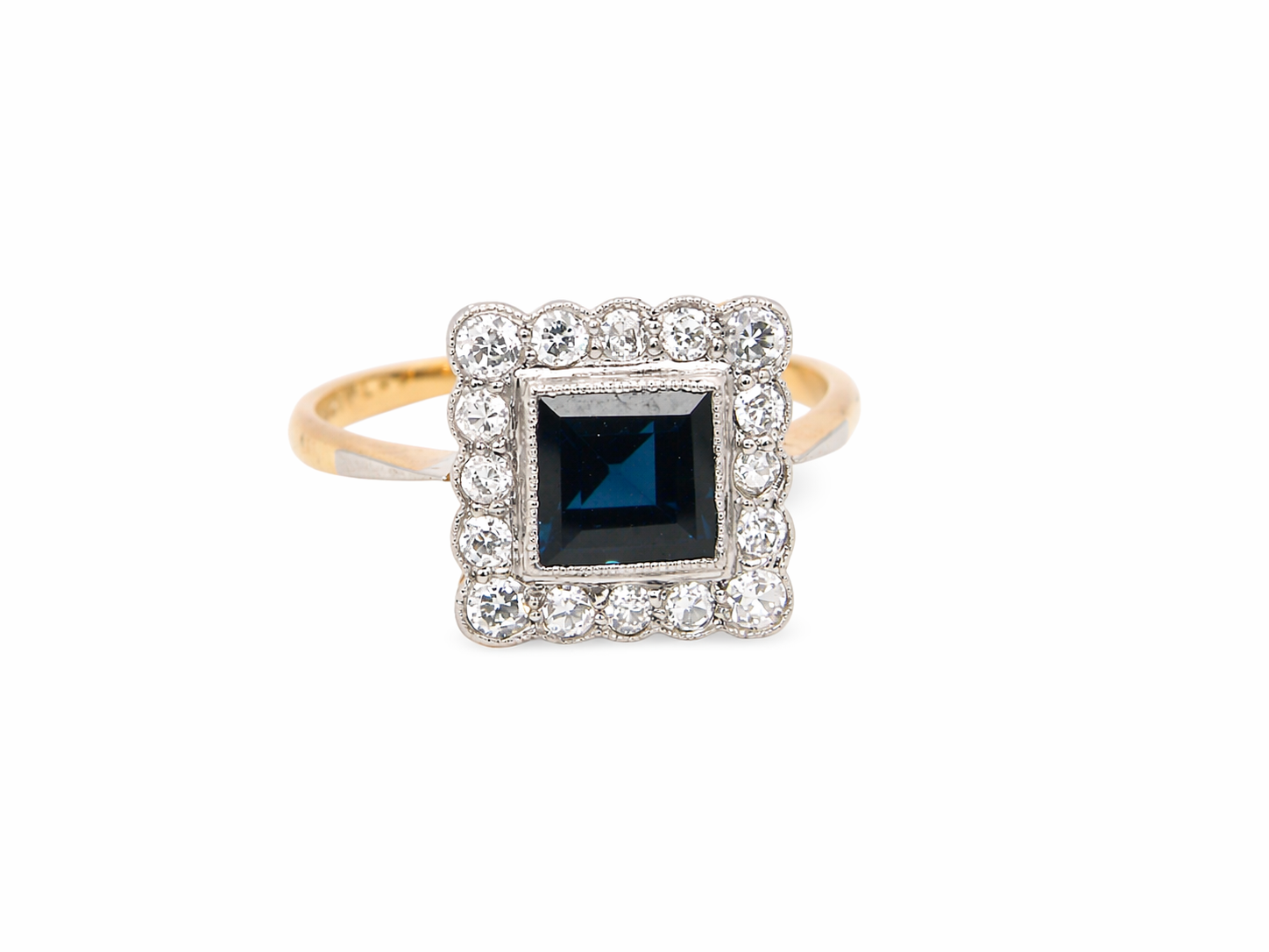A mid 20th century cluster ring. Features a square dark blue sapphire 5x5mm (est 0.60 carats) mille grain setting in platinum.&nbsp;
