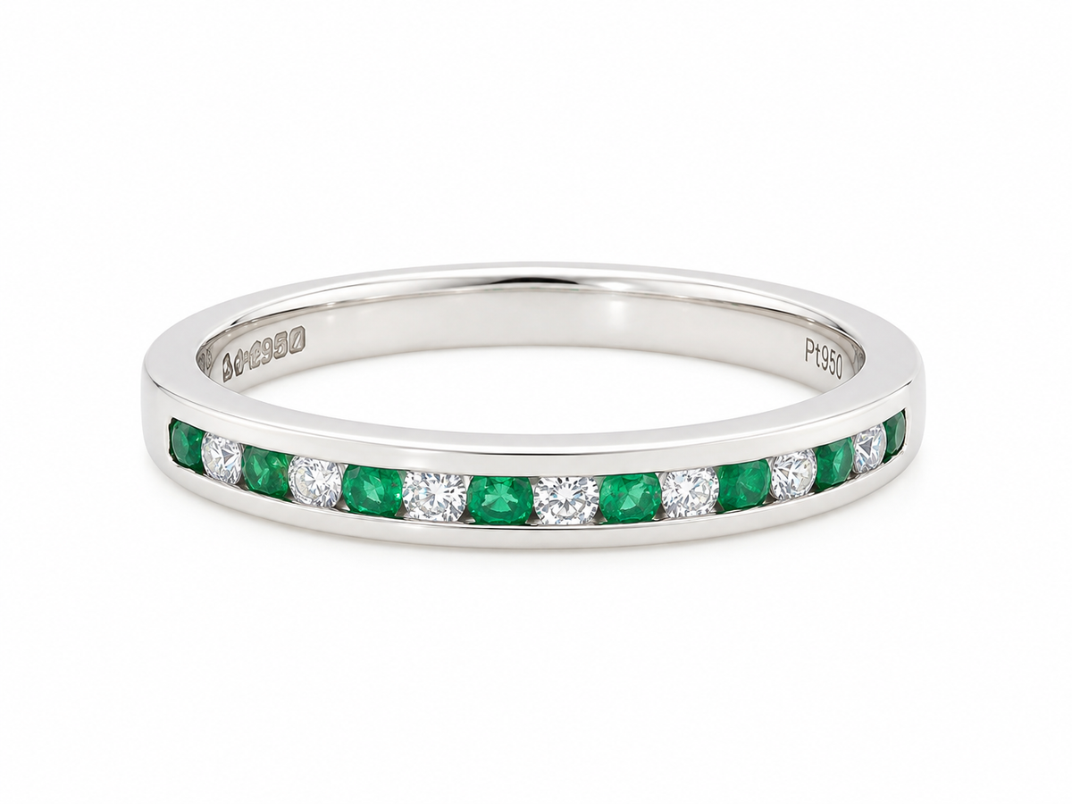 A ring featuring a channel setting of round-cut green emeralds and clear diamonds, shown on a plain white background.