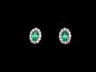 A pair of oval stud earrings featuring marquise-cut green emeralds surrounded by small clear stones in a silver-toned setting, presented on a solid black background.