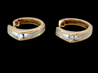 A pair of gold huggie hoop earrings with a silver inlay and a small clear gemstone on each earring, shown against a solid black background.