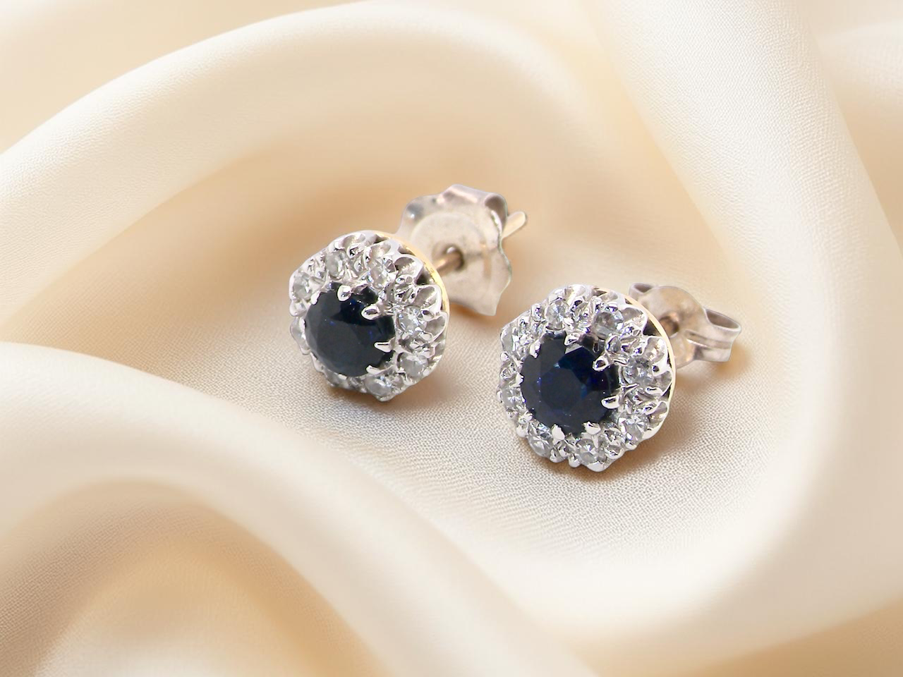 A pair of stud cluster earrings. Each earring is set with a dark blue sapphire centre .

Measures 4mm, surrounded by an outer halo of 1.3mm diamonds 