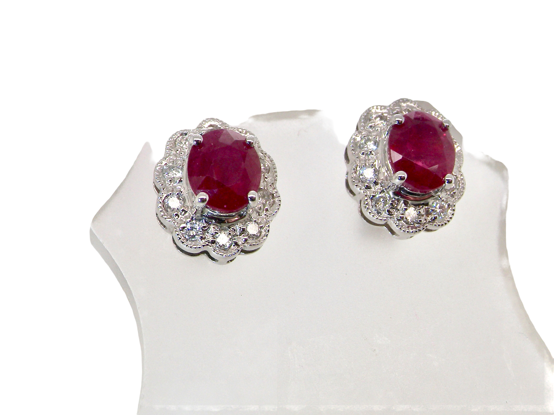 A pair of white gold earrings, each set with an oval ruby 6x4.9mm (est 0.60 carats) complimented by an outer halo of ten  diamonds