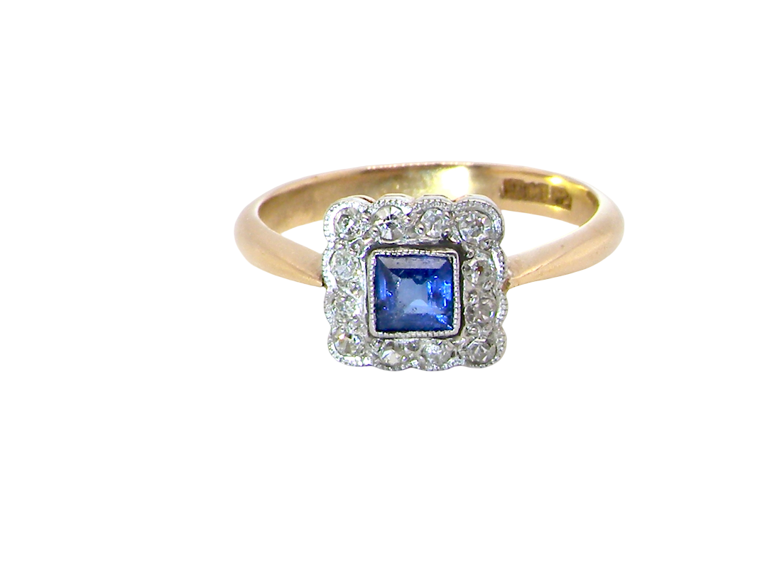 A pretty square cluster ring. Features to the centre a cornflower blue square sapphire, 4x4mm (est 0.30 carats) mille grain set.

Complimented by a halo of twelve x 1.5 mm single cut white diamonds 