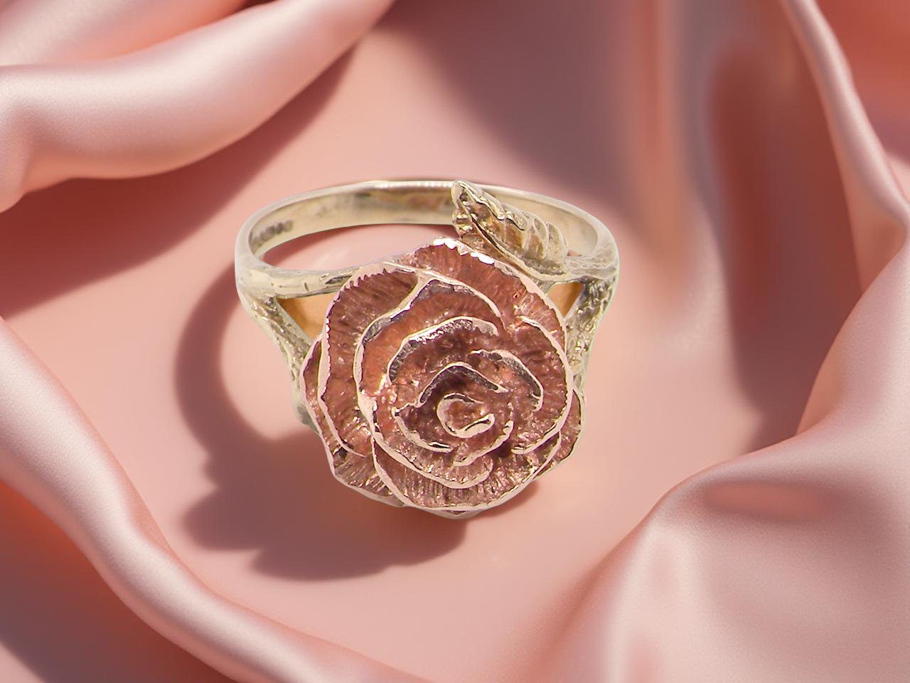 Gold ring with rose design on a pink fabric background