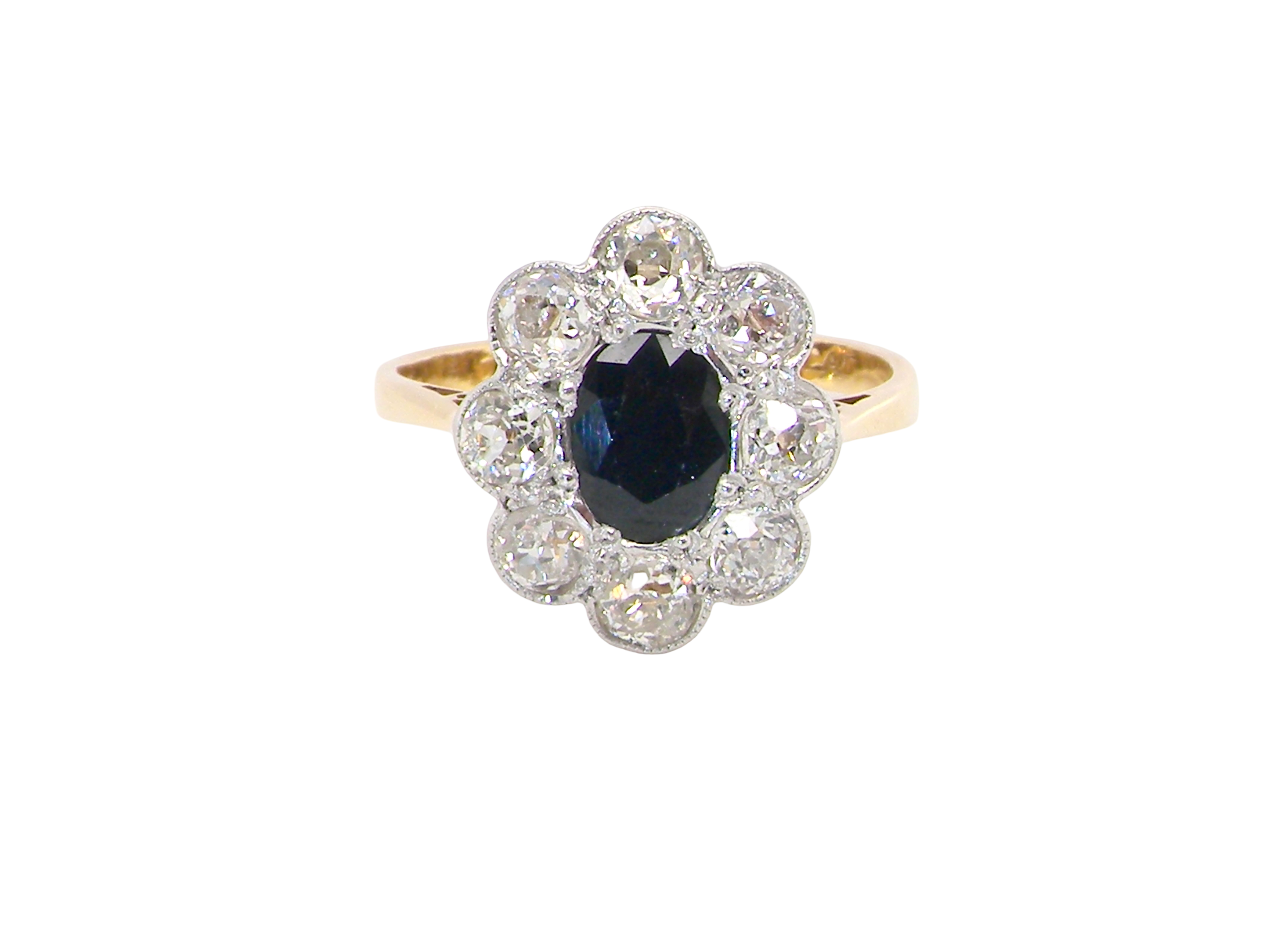 A striking vintage sapphire and diamond cluster ring dating from the 1930s–1940s, beautifully crafted in platinum and 18 carat gold. At the centre sits a richly coloured oval-cut sapphire of deep inky blue-black hue, measuring approximately 7 x 5mm 