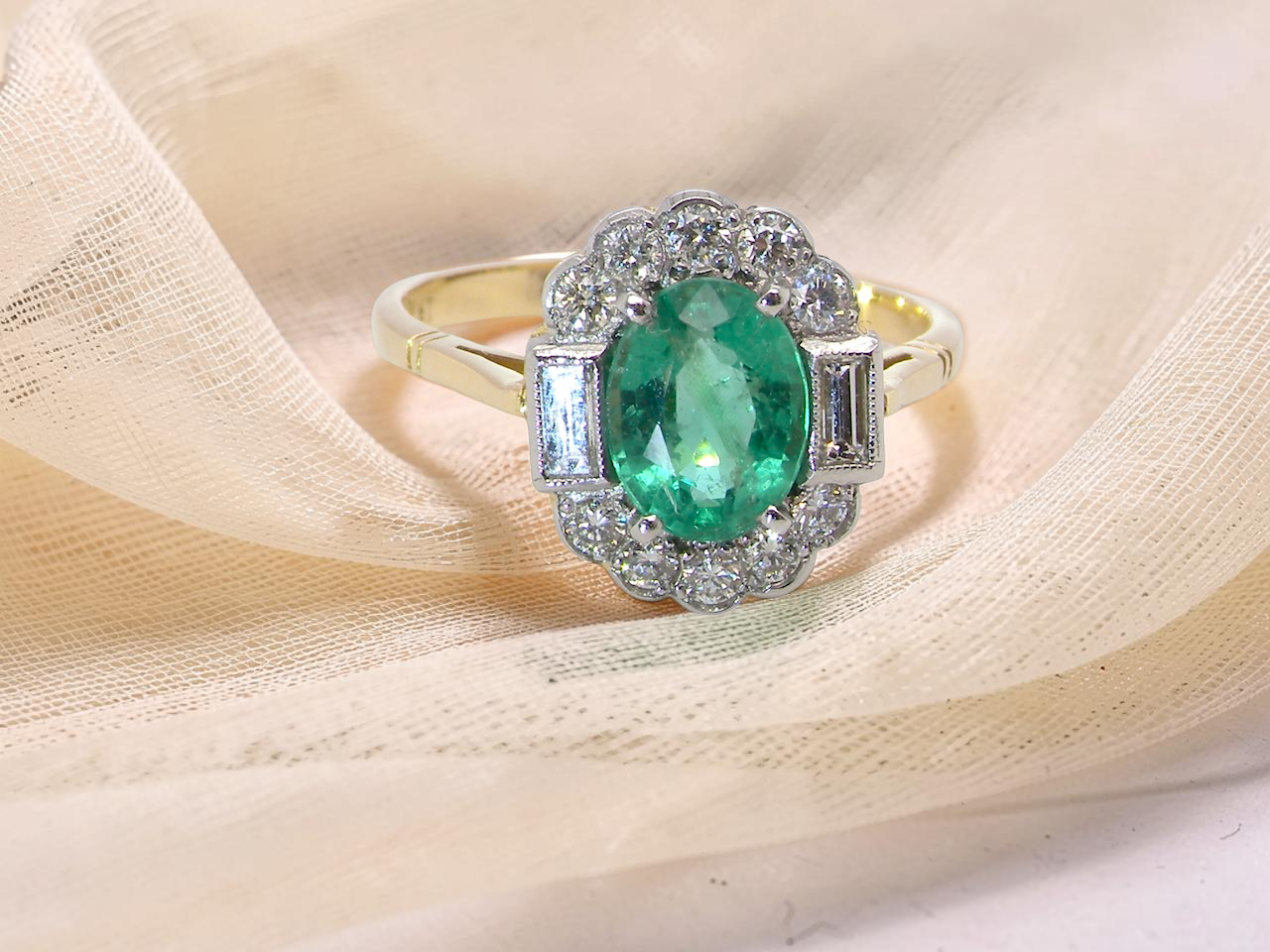 A stunning vintage cluster ring, set with an oval-cut emerald measuring 8 x 6mm, approximately 1.10 carats. The emerald displays a rich, deep grass-green colour with natural inclusions,