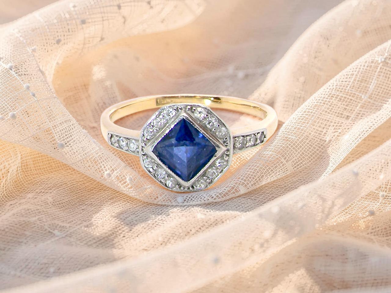 A very pretty Art Deco cluster ring. To the centre a mid to dark blue sapphire, square cut but set as a 'diamond shape'. Measures 5x5mm, 