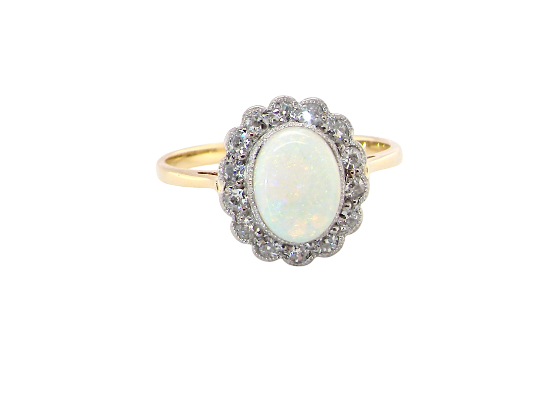 A yellow gold ring featuring a central oval white opal surrounded by a halo of small clear stones, set against a plain white background.