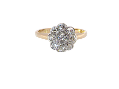 A vintage-style cluster ring featuring a central cluster of round diamonds in a silver-toned setting, mounted on a yellow gold band, shown against a plain white background.