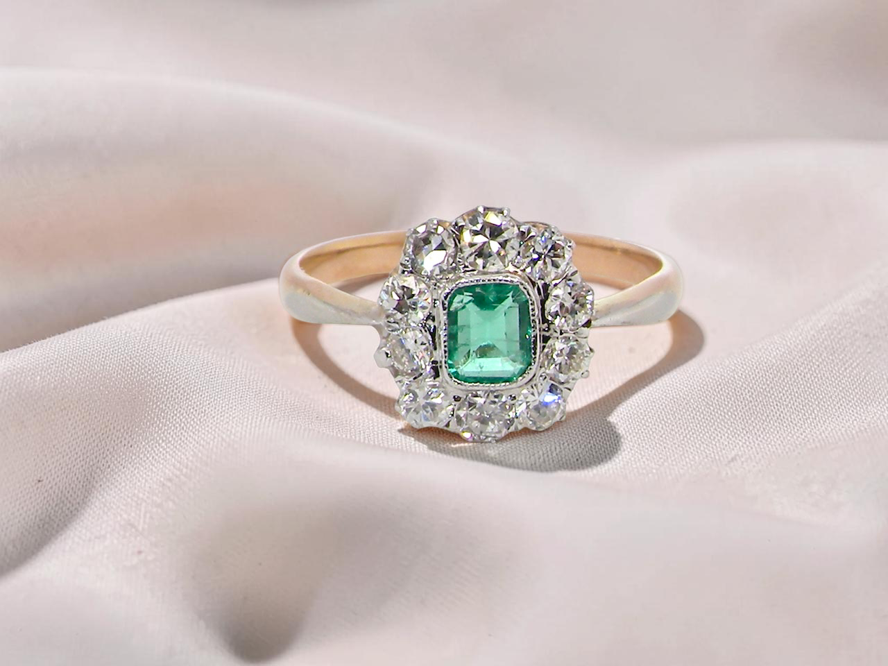  cluster ring, the centre stone a cushion shaped emerald 4x3.5mm, mid to dark green colour. Mille grain setting.
