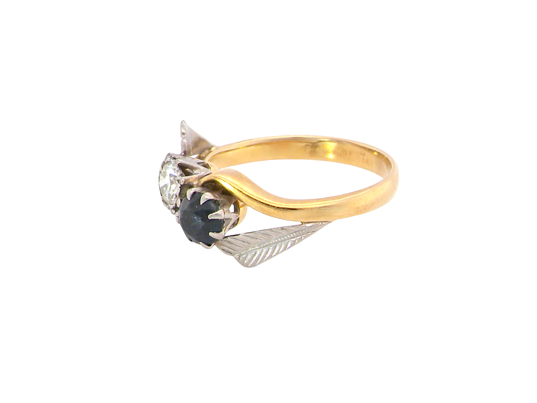 A vintage-style gold ring with a curved yellow gold band, a clear round gemstone, and a central black oval gemstone surrounded by textured silver-toned leaf-like settings, shown on a plain white background.