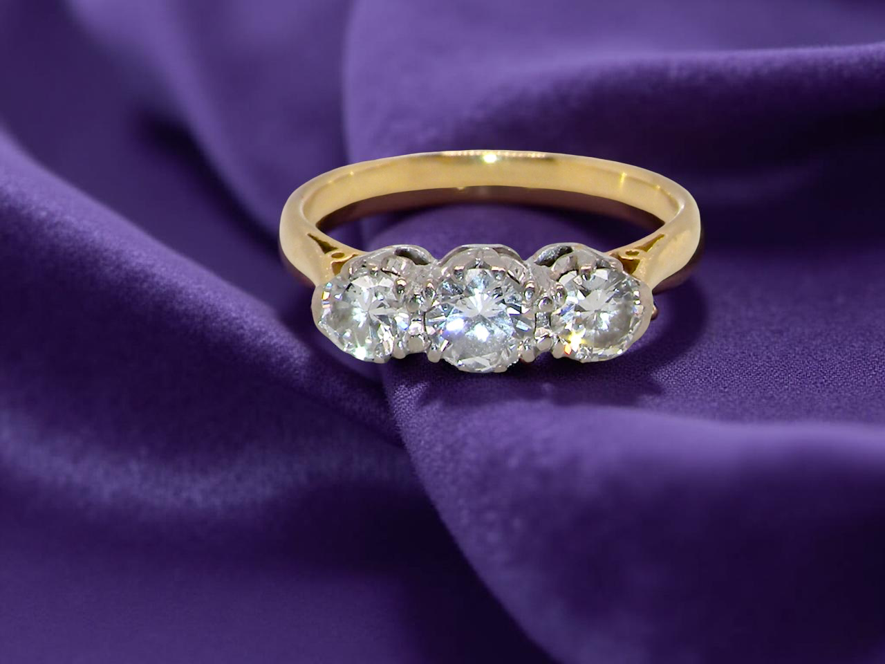 Gold ring with three diamonds on a purple fabric background