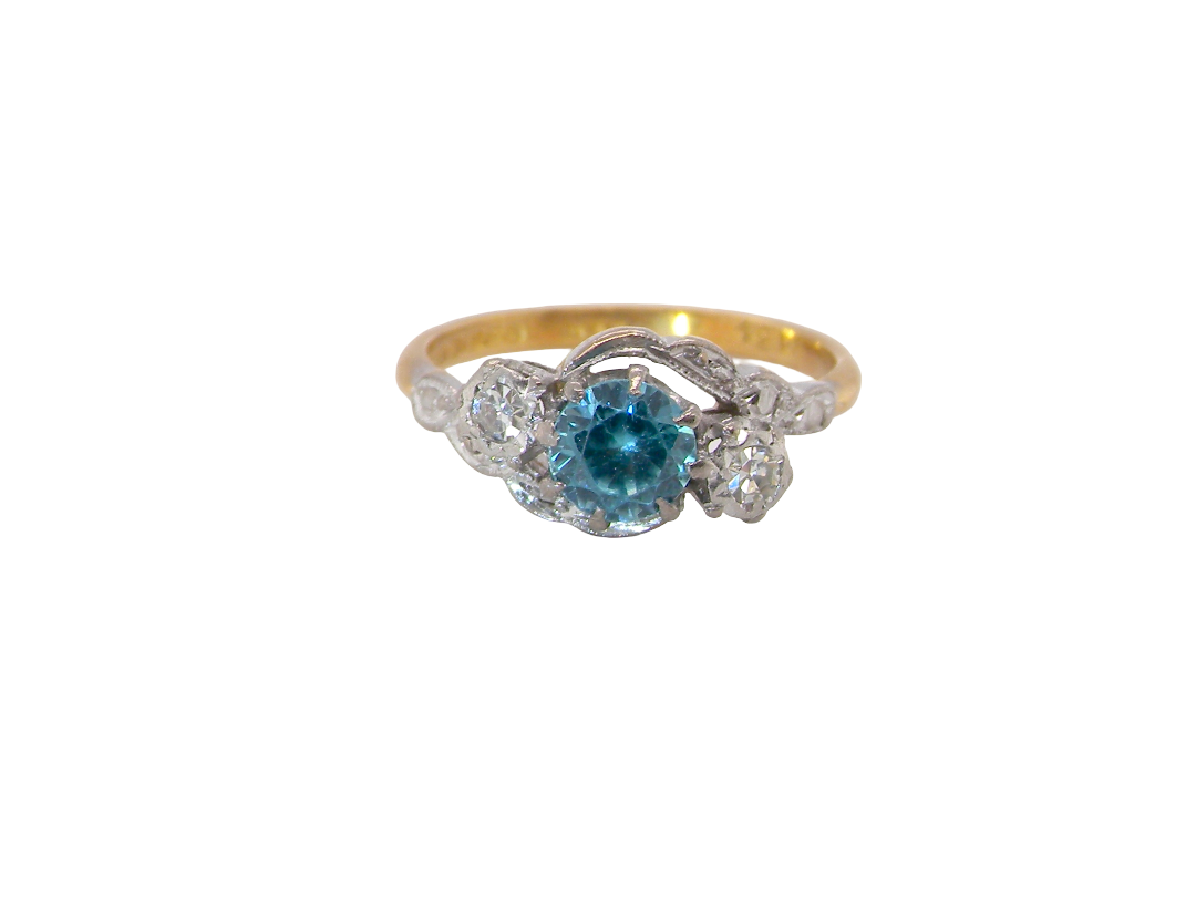 A vintage three stone ring, cross over style and features a round 6mm&nbsp; natural blue zircon centre stone