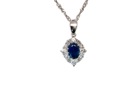 A white gold pendant. The centre stone an inky black blue sapphire 7x5mm, claw set. Complimented by an outer halo of twelve brilliant cut white diamonds.