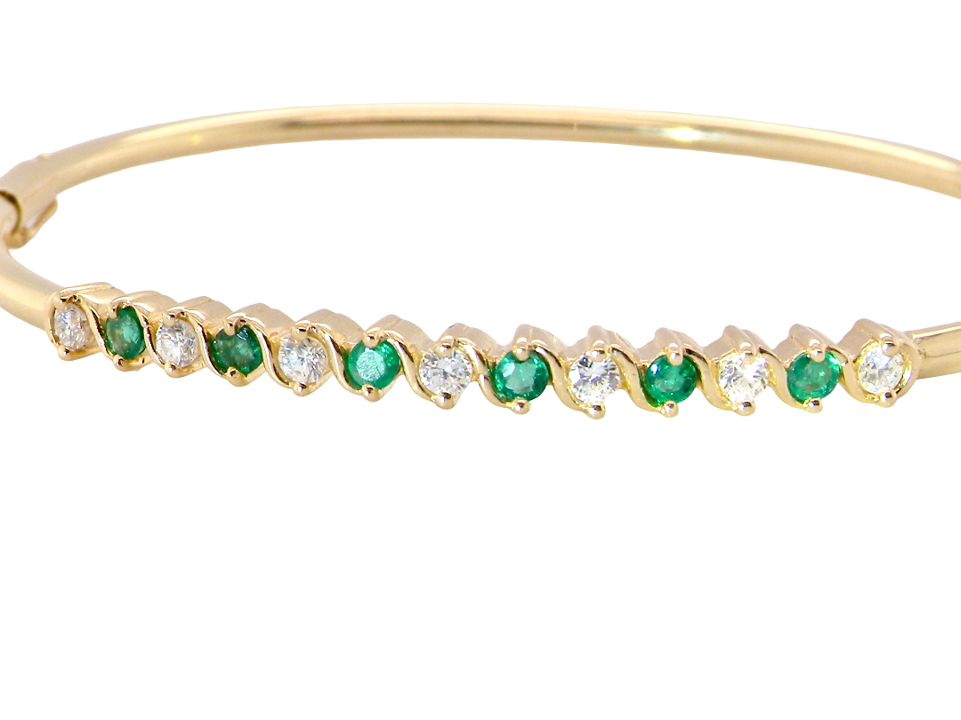 A yellow gold bangle. Features alternate emeralds and diamonds. Six 2.7mm emeralds and seven brilliant cut white diamonds, each 2.7mm 
