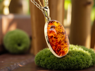 Amber pendant necklace on a stand with a blurred natural background