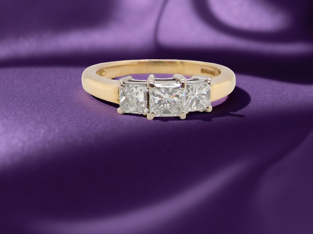 Gold ring with three diamonds on a purple fabric background