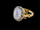 An 18 carat gold cluster ring. Features an oval opal centre stone with excellent play of colour with a predominance of watery purple and flashes of orange, 
Measures 11x7mm.