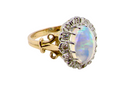 An 18 carat gold cluster ring. Features an oval opal centre stone with excellent play of colour with a predominance of watery purple and flashes of orange, and luminous green.
Measures 11x7mm. side