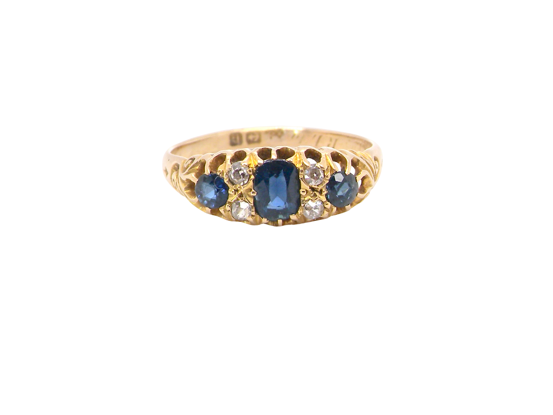 A yellow gold ring featuring a central oval-cut blue sapphire flanked by smaller round-cut blue sapphires and clear diamonds, set against a plain white background.