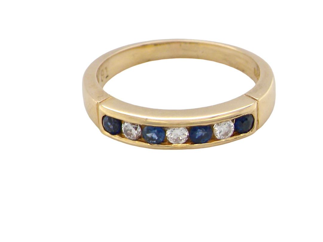A yellow gold eternity ring featuring a row of round-cut dark blue sapphires and clear round diamonds set in a polished band, shown on a plain white background.