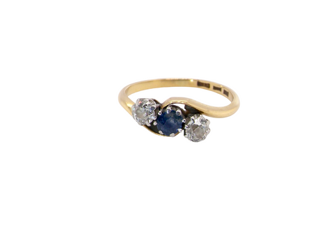 An 18 carat gold three stone cross over ring.

Centre stone a round sapphire 4mm diameter. Each side a brilliant cut white diamond 4mm diameter (0.25 carats estimated), colour i-k, clarity Si.