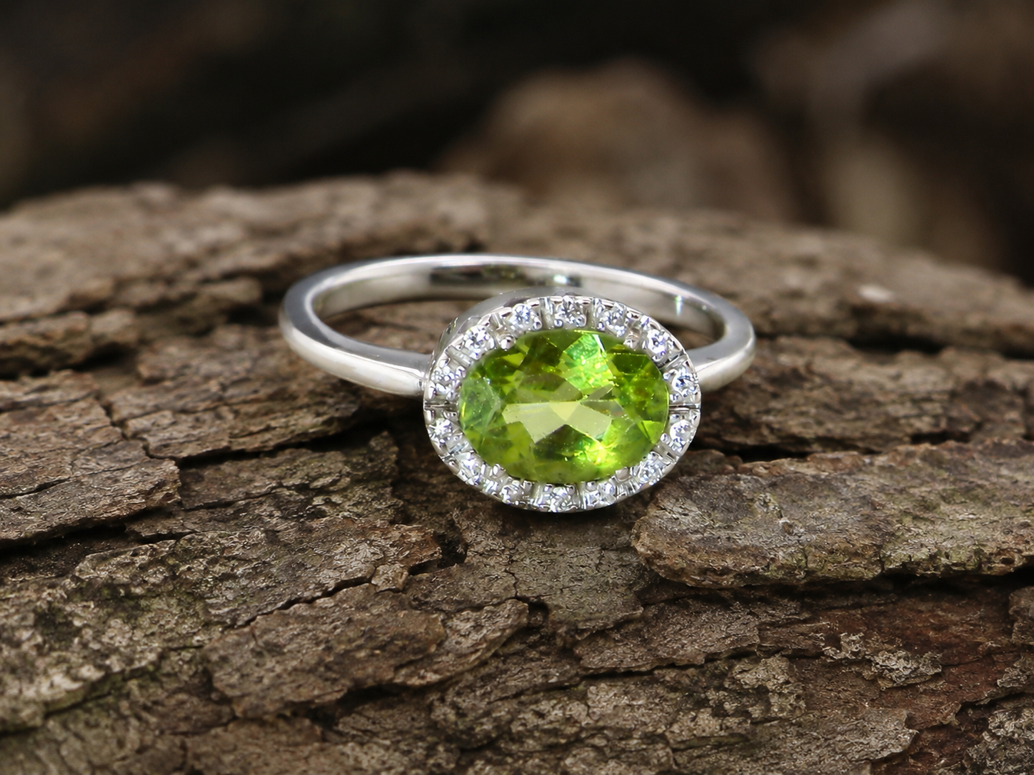 An 18 carat white gold* cluster ring. Features and oval shaped peridot  measures 8.5x6.5mm.
