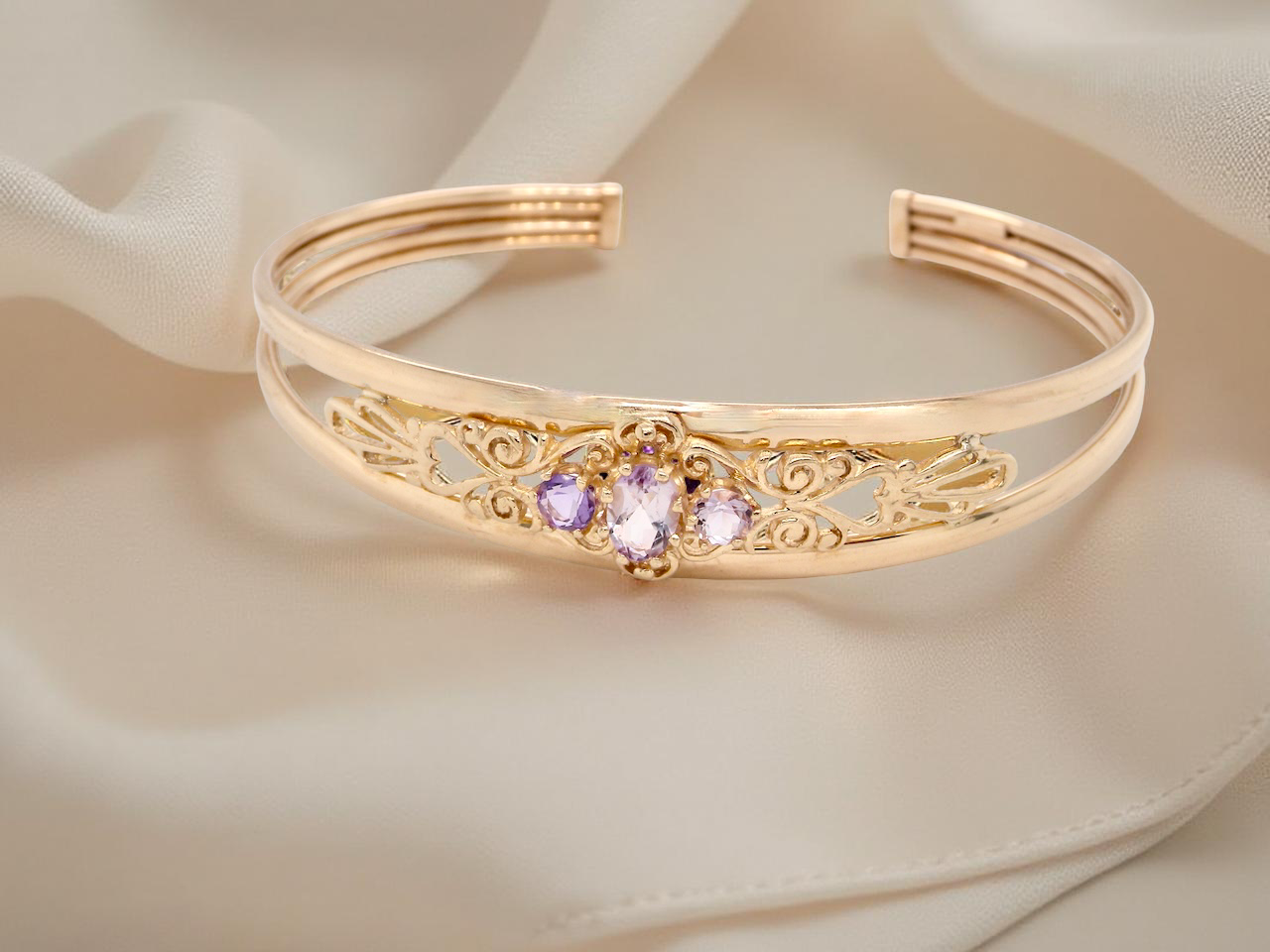 Gold bracelet with decorative elements and gemstones on a soft beige fabric background