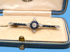 An Edwardian bar brooch. The centre 'target' style portion is set with a brilliant cut white diamond 4mm (0.25 carats) colour H-j, . Mille grain setting.