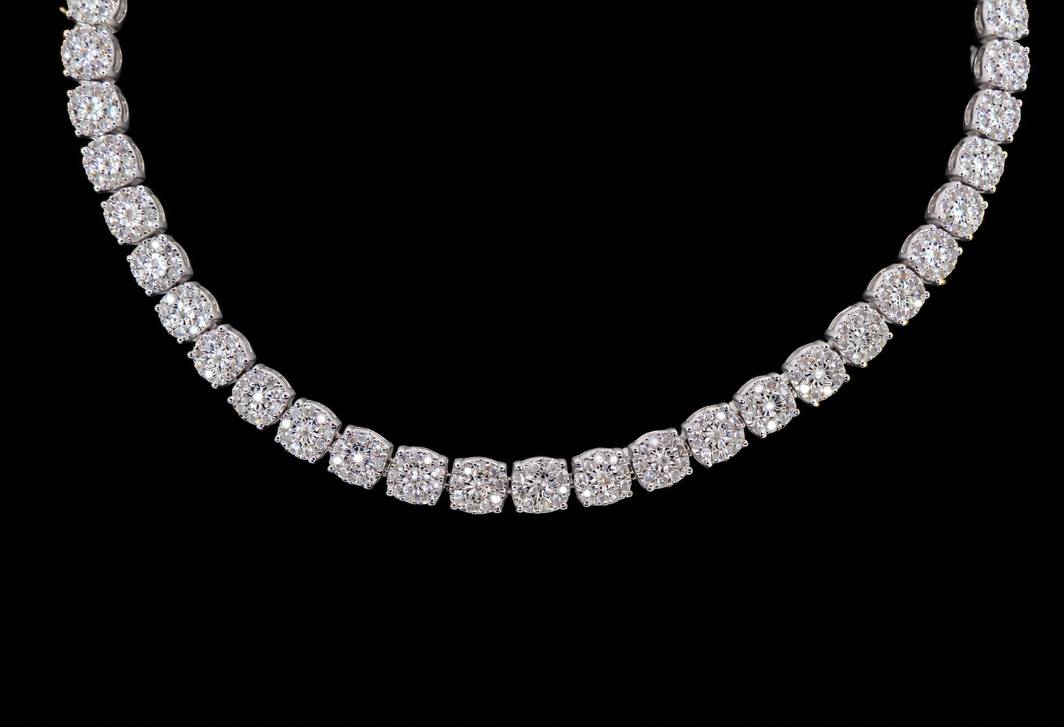A diamond tennis necklace with cushion-cut diamonds set in a silver-toned metal, shown against a solid black background.