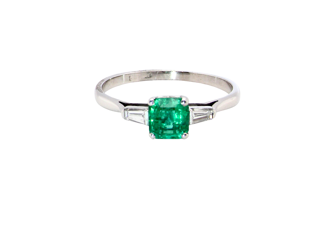 An elegant and timeless platinum ring featuring a stunning step-cut emerald to the centre, measuring approximately 5.5 x 5.5mm and estimated at 0.80 carats. The emerald displays a vibrant, deep green colour 