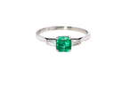 An elegant and timeless platinum ring featuring a stunning step-cut emerald to the centre, measuring approximately 5.5 x 5.5mm and estimated at 0.80 carats. The emerald displays a vibrant, deep green colour 