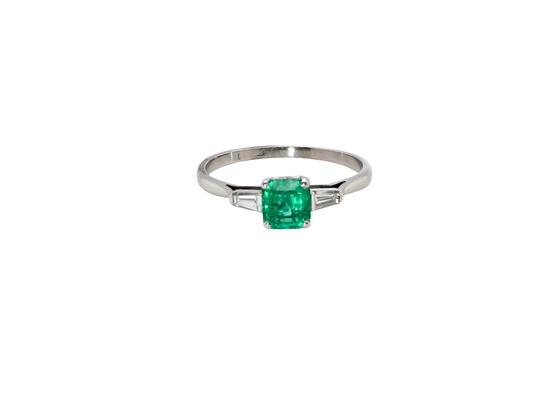 An elegant and timeless platinum ring featuring a stunning step-cut emerald to the centre, measuring approximately 5.5 x 5.5mm and estimated at 0.80 carats. The emerald displays a vibrant, deep green colour with excellent presence.