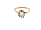 An elegant&nbsp; cluster ring featuring a white opal centre stone measuring 6 × 4mm, displaying a lively and attractive play of colour.