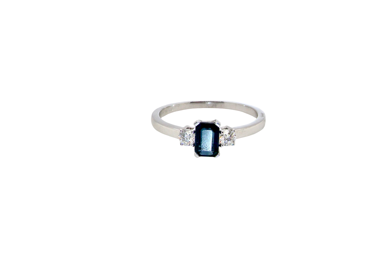 An elegant three-stone ring crafted in 18 carat white gold, featuring a striking rectangular dark blue sapphire at the centre, measuring 6 × 4 mm and weighing approximately 0.50 carats.