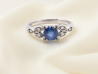 An elegant vintage-style platinum ring showcasing a beautifully proportioned round sapphire with a soft mid to light cornflower blue hue. The sapphire measures 5.6mm in diameter 