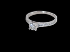 A diamond engagement ring with a round center stone and pavé-set diamonds on the band, shown against a solid black background.