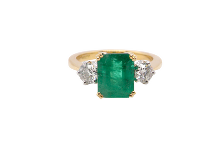 An exceptional three-stone ring featuring a vibrant step-cut emerald to the centre, measuring 8.6 x 7.0mm and weighing approximately 2.10 carats. The emerald displays a beautiful grass-green colour 