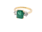 An exceptional three-stone ring featuring a vibrant step-cut emerald to the centre, measuring 8.6 x 7.0mm and weighing approximately 2.10 carats. The emerald displays a beautiful grass-green colour and is secured in a  four-claw setting.