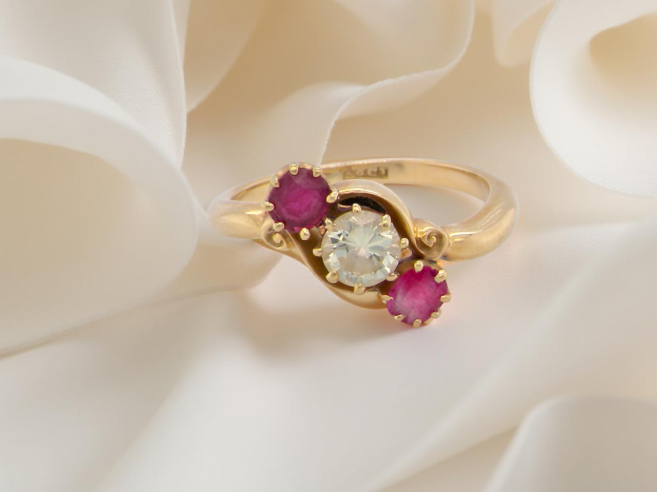 Gold ring with a central diamond and two rubies on a white fabric background