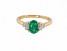 A yellow gold ring featuring an oval-cut green emerald center stone, flanked by small clusters of clear pavé diamonds, set against a plain white background.