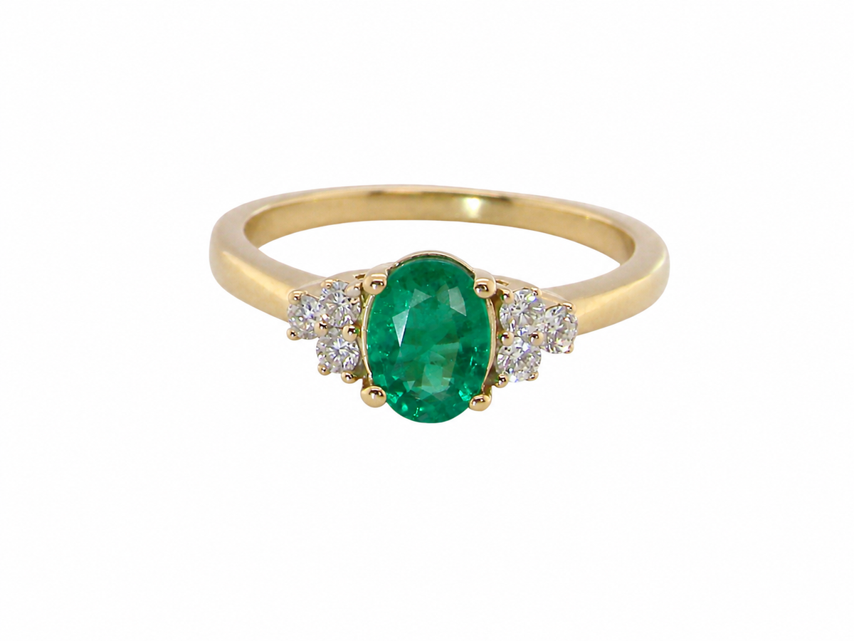 A yellow gold ring featuring an oval-cut green emerald center stone, flanked by small clusters of clear pavé diamonds, set against a plain white background.