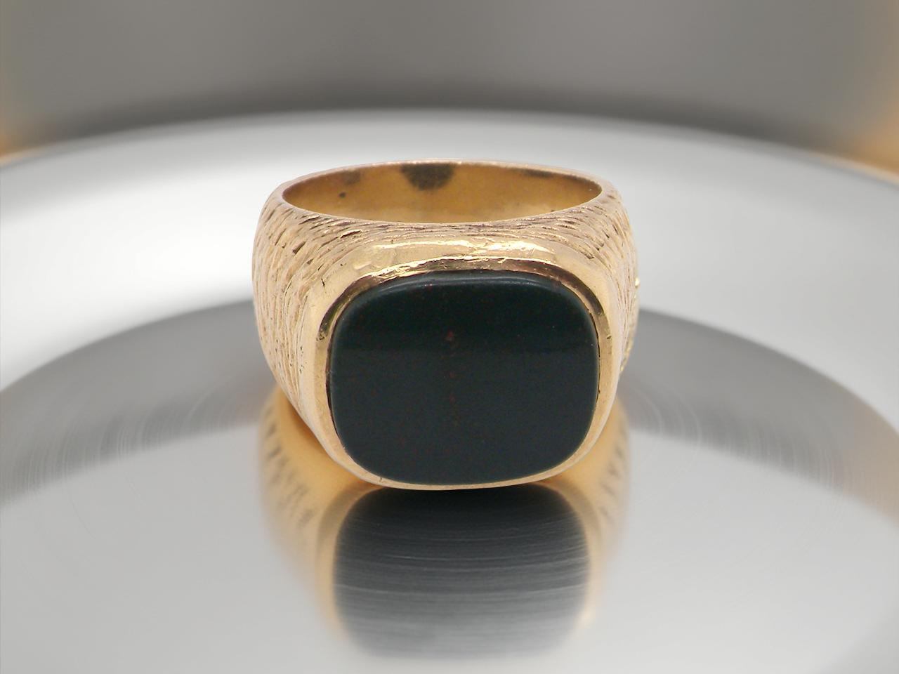 Gold ring with a black stone on a reflective surface