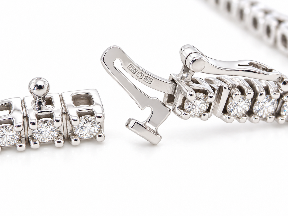 Close-up of a silver-toned tennis bracelet showing the clasp mechanism and a section of the linked chain with clear gemstones on a white background.