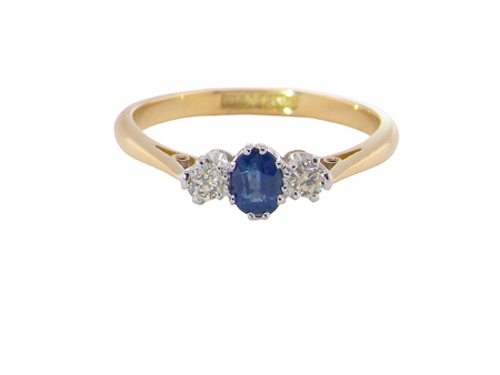 The classic trilogy ring, this features to the centre a round mid to dark blue sapphire and each side a brilliant cut white diamond