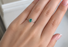 White gold ring with a green gemstone on a person's finger against a neutral background
