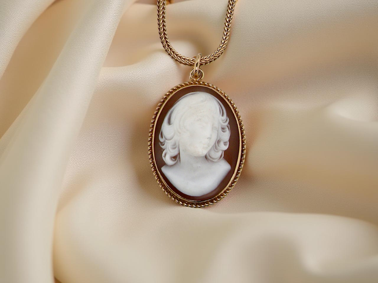Vintage-style cameo pendant on a gold chain against a soft beige background